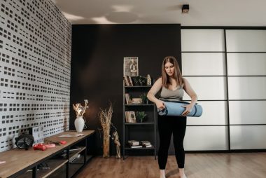 Plus size woman rolling a yoga mat in a stylish indoor setting with modern decor.